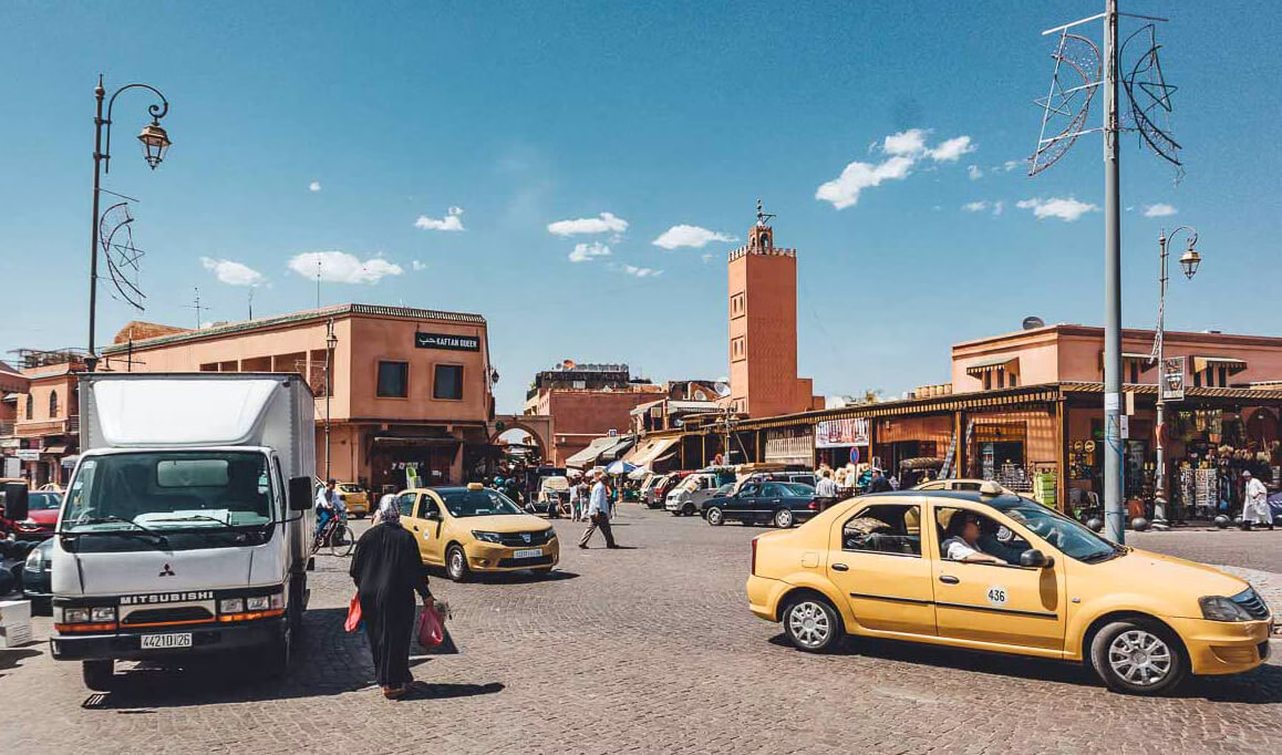 Un pequeño taxi beige de Marrakech aparcado cerca de la medina con el conductor esperando.